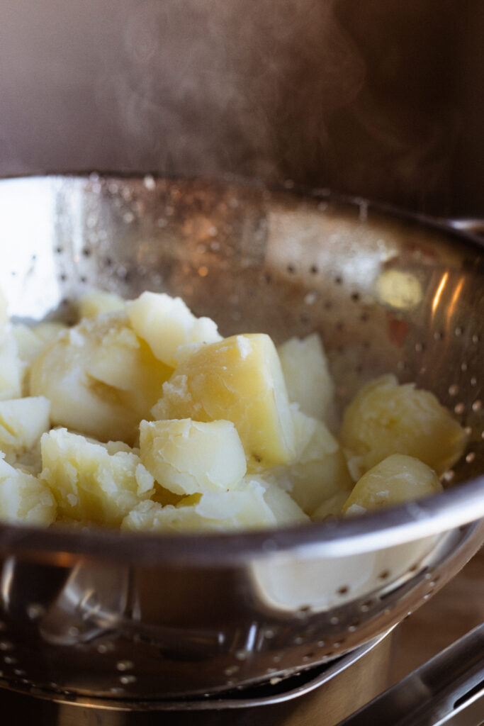 Tender steaming boiled potatoes rest on a metal colander.