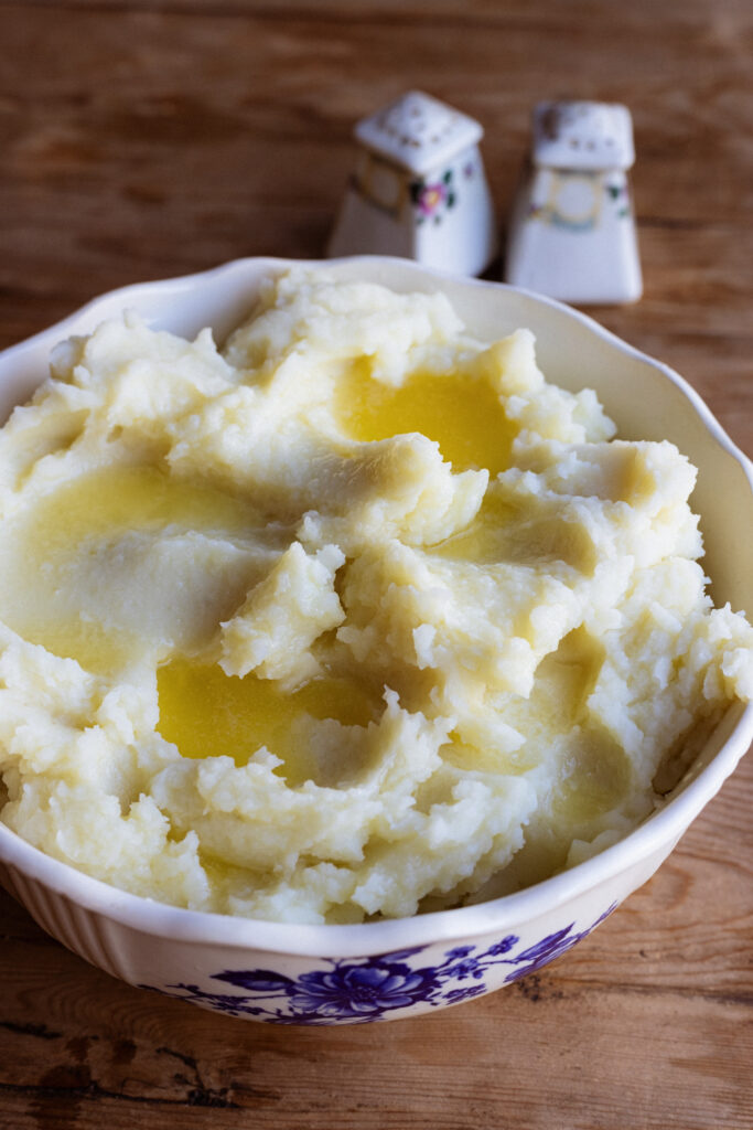 Light and fluffy mashed potatoes are topped with melted butter and served in a ceramic dish.