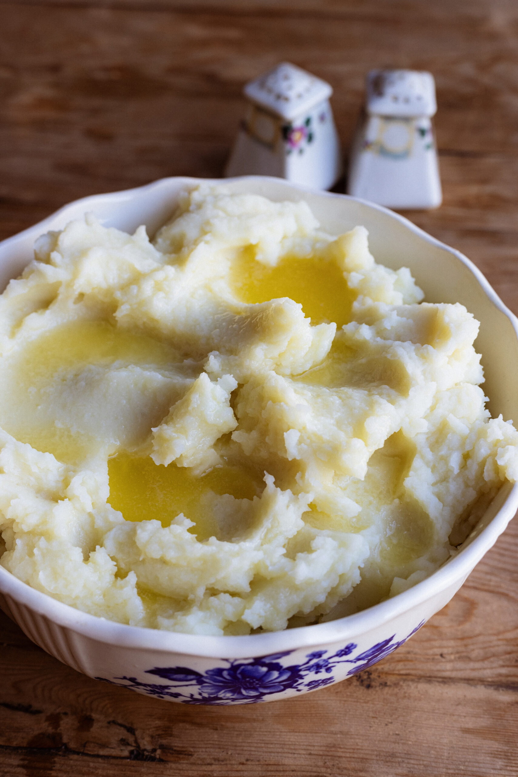 A large bowl of fluffy mashed potatoes topped with pools of melted butter.