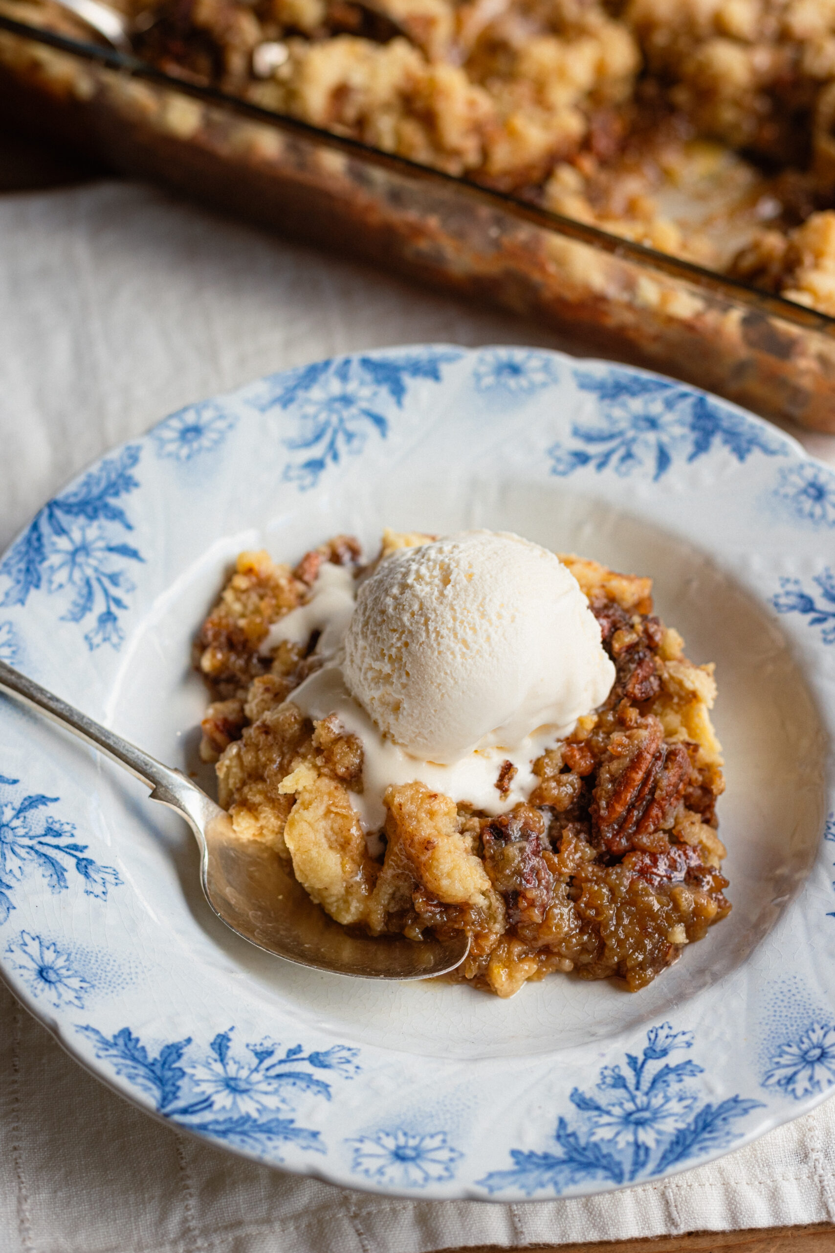 A bowl of warm pecan pie butter cake topped with a scoop of vanilla ice cream.