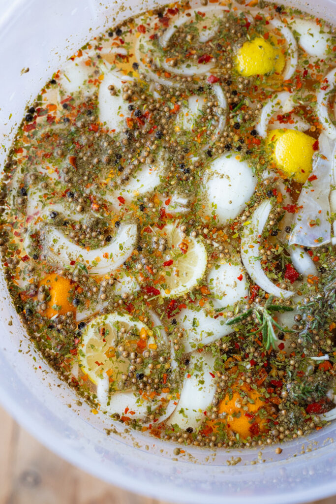 A close-up overhead image of a large tub filled with an organic turkey brine made with herbs, spices, onions, and citrus.