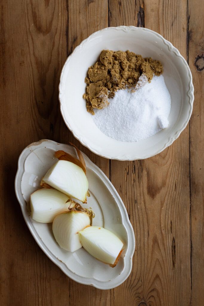 Two platters hold ingredients for an easy turkey brine -- a small bowl holds a mixture of salt and brown sugar, and a second plate holds a quartered onion.