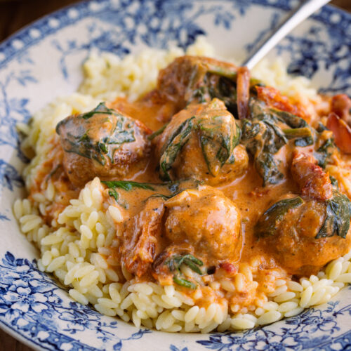 Close up of chicken meatballs in orange sauce over orzo pasta in a blue/white bowl.