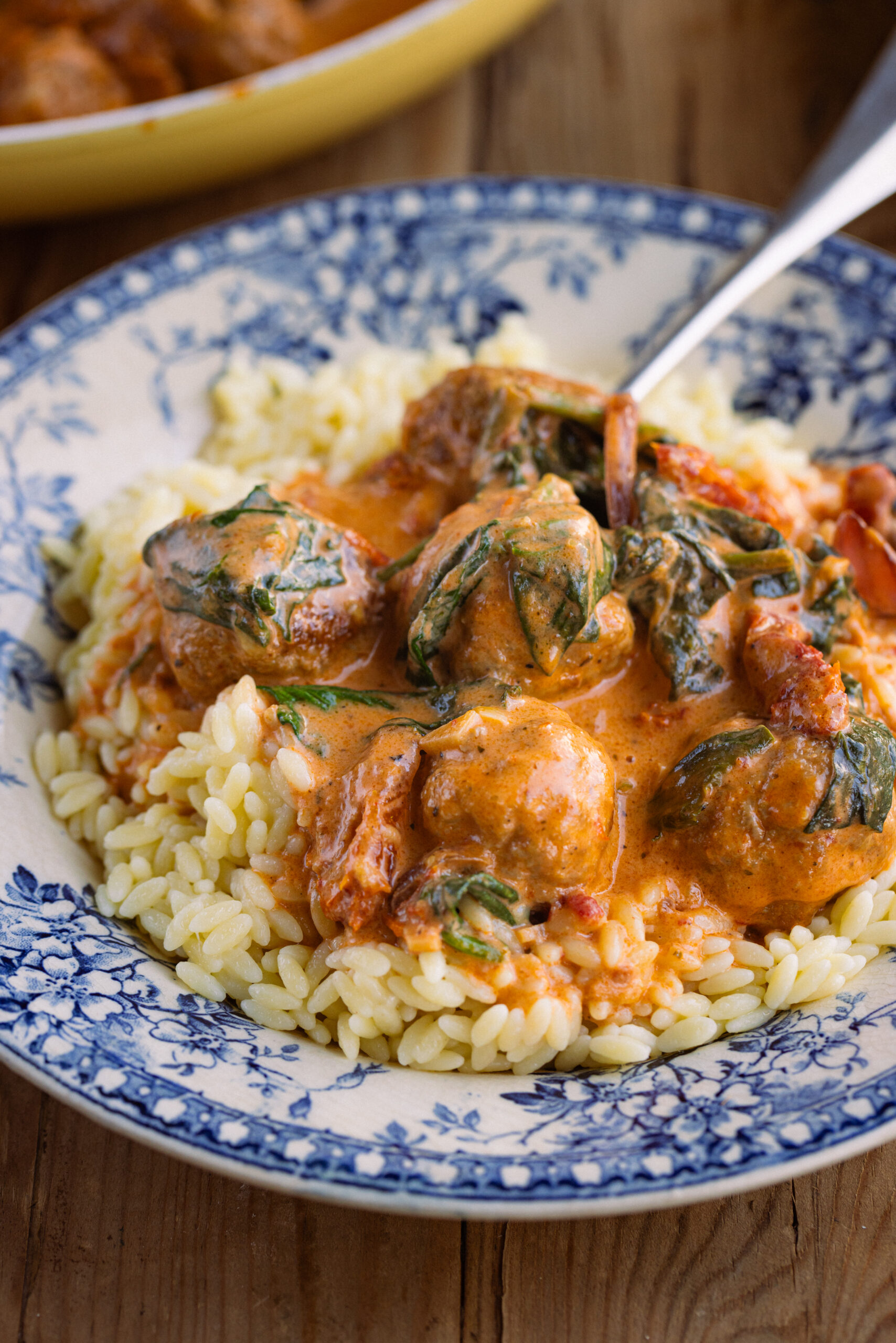 Close up of chicken meatballs in orange sauce over orzo pasta in a blue/white bowl.